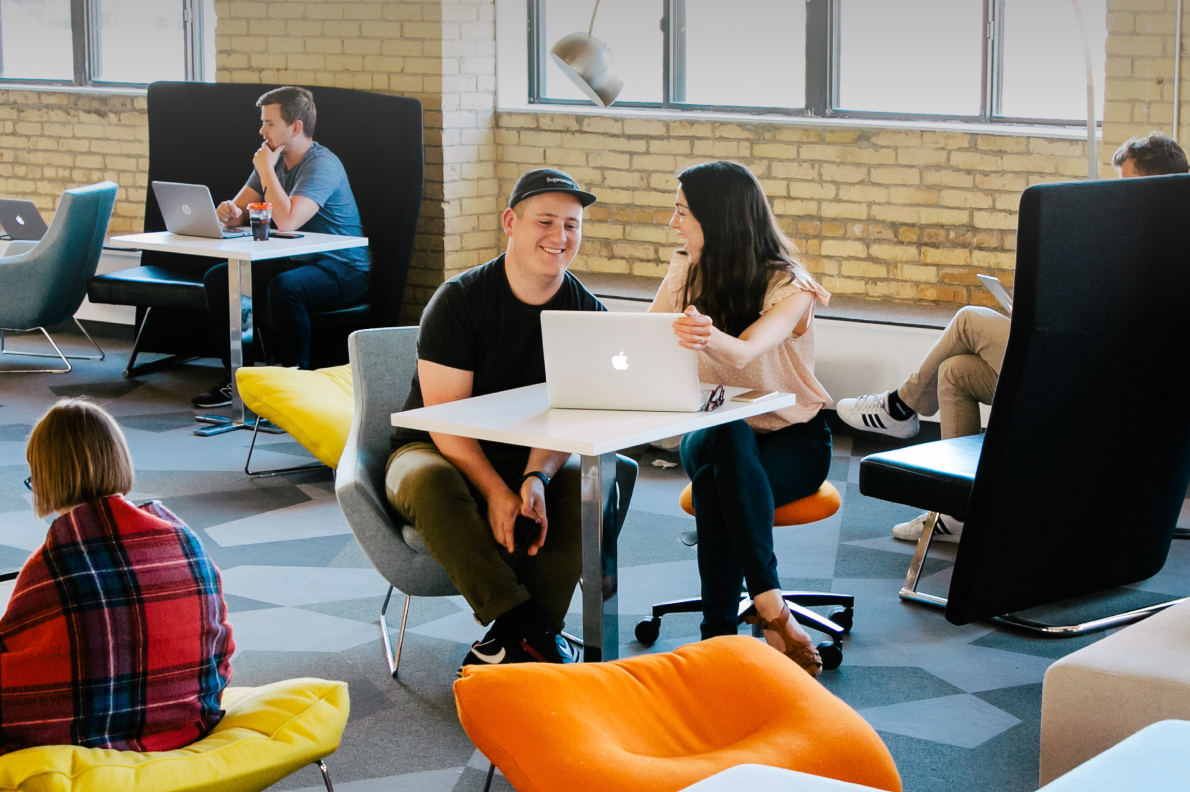 Adam sat with fellow designer Kristina in a modern office space discussing work in front of a laptop.
